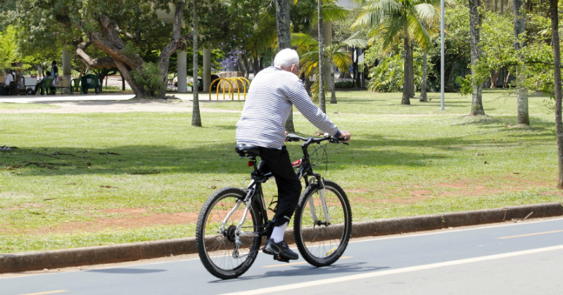 Imagem de um idoso pedalando uma bicicleta num parque