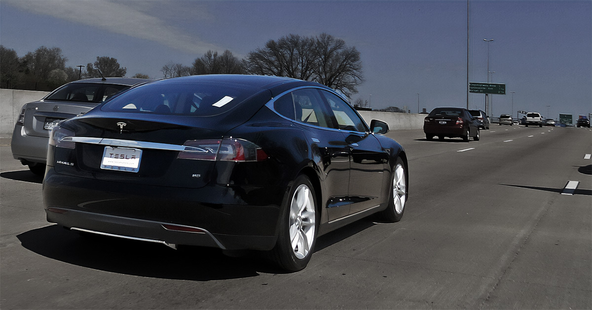 Carro autônomo da Tesla trafegando em uma rodovia, cercado por outros veículos.